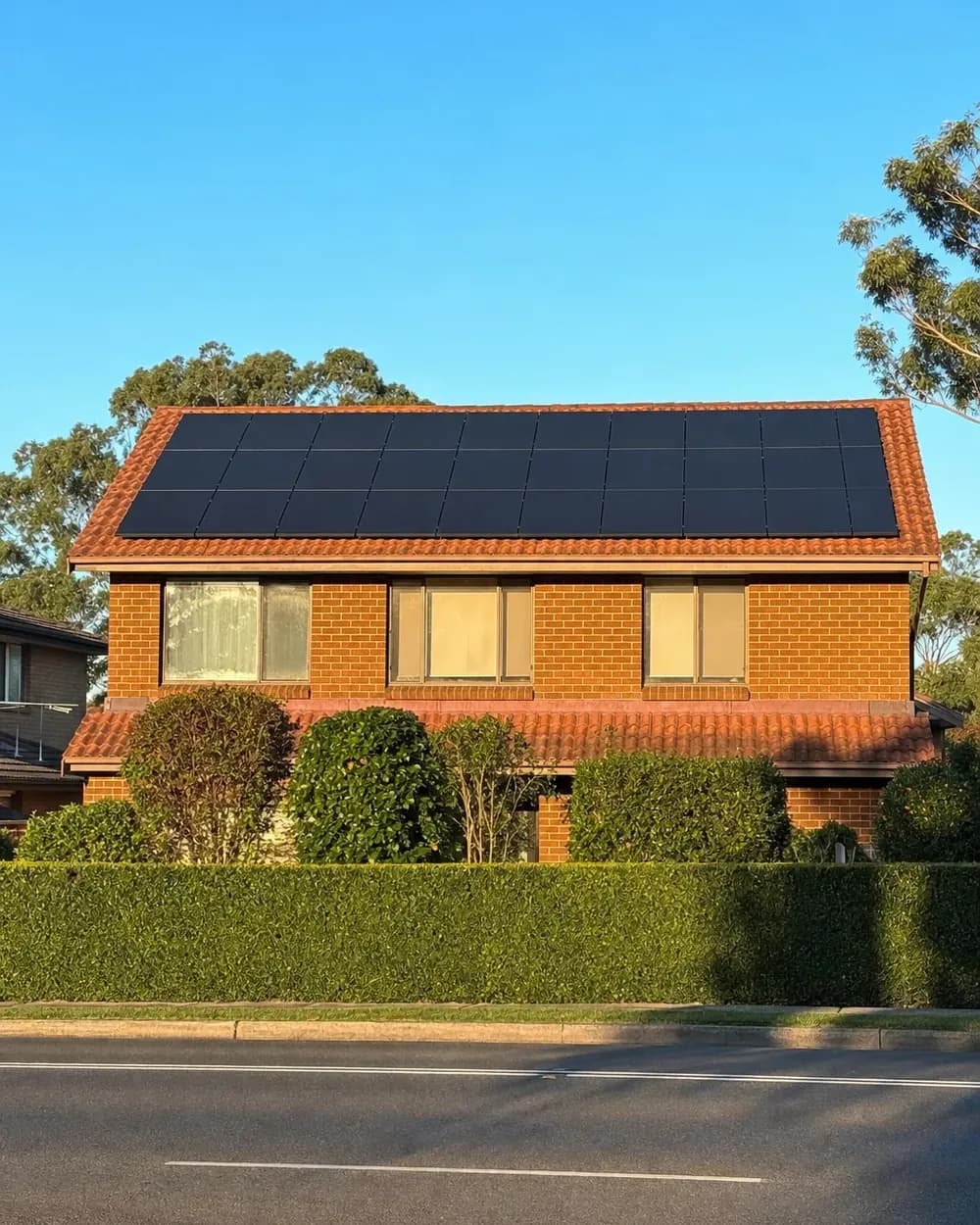 A brick Western Sydney home with a full-width array of black solar panels covering its tiled roof
