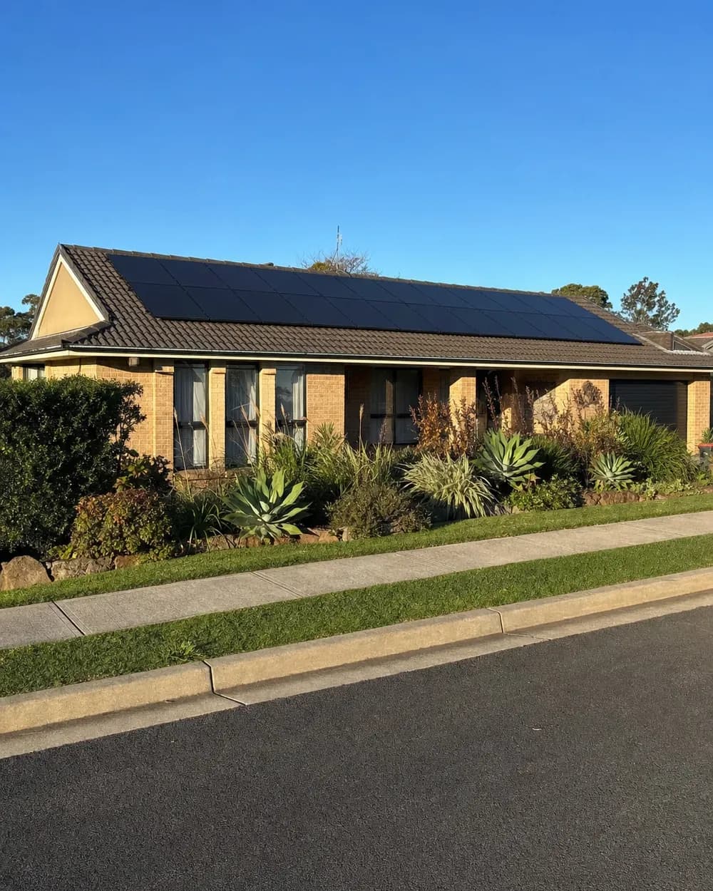 A low-set Western Sydney brick home with black solar panels running the length of its dark tiled roof